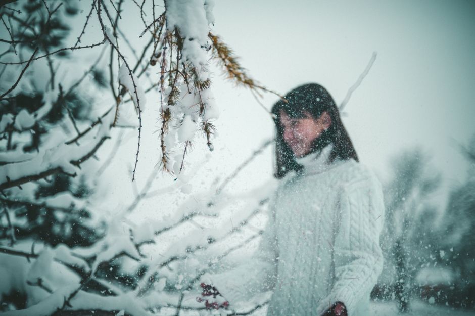 Woman in cozy sweater enjoying the winter snowfall in a Ukrainian forest.