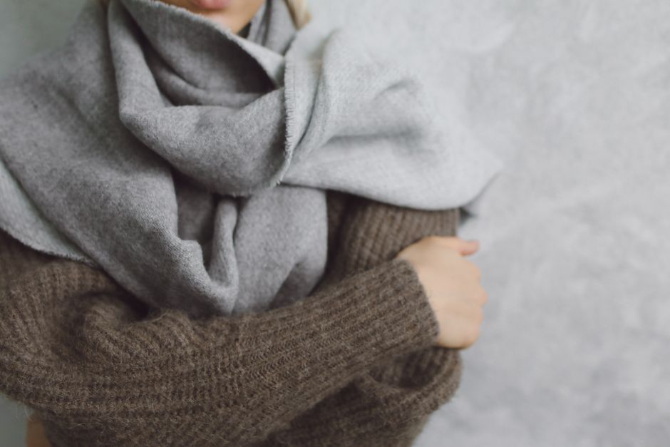 Close-up of a person wearing a grey scarf and brown knitted sweater. Ideal for winter fashion themes.
